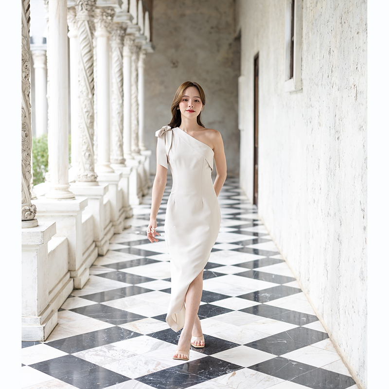 kudapy เดรสยาวสีชมพู/สีครีม/สีน้ำตาลอมส้ม ช่วงบนเป็นแบบปาดไหล่ข้างเดียวแต่งผ้าพับอก มีสายผูกโบว์ที่ไหล่ด้านขวาเพิ่มความหวาน เป็นกระโปรงทรงสอบ กระโปรงชายเฉียงเพิ่มความสวยชิค