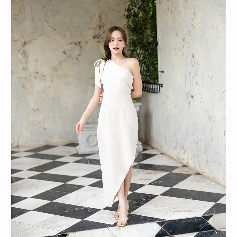 kudapy เดรสยาสีสีน้ำตาลอมส้ม/สีครีม ช่วงบนเป็นแบบปาดไหล่ข้างเดียวแต่งผ้าพับอกดูไม่เรียบจนเกินไป มีสายผูกโบว์ที่ไหล่ด้านขวาเพิ่มความหวาน