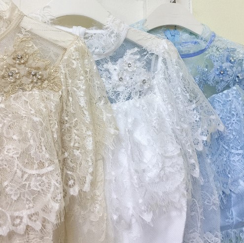 kudapy เสื้อลูกไม้เนื้อนิ่มสีขาว/ชมพู/ครีมทอง/ฟ้า แขนยาว คอปิด ระบายรอบไหล่เย็บแต่งดอกไม้สามมิติช่วงไหล่ด้านหน้า เอวระบายบาน ผ้าลูกไม้นิ่มยืดหยุ่นเนื้อเงา