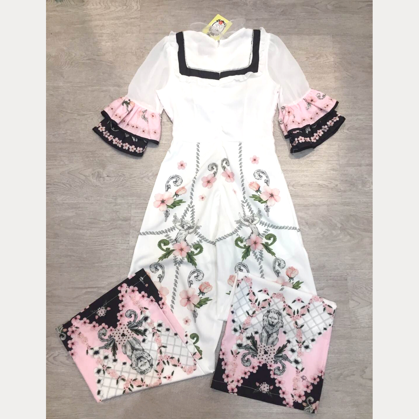 kudapy จั๊มสูทขายาวสีครีมตัดชมพู คอกลมระบายด้วยผ้าแก้วรอบคอ ช่วงแขนระบายสองขั้น พิมพ์ลายรอบตัว มีซับในและซิปหลัง