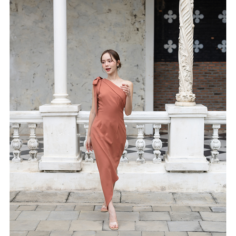 kudapy เดรสยาวสีชมพู/สีครีม/สีน้ำตาลอมส้ม ช่วงบนเป็นแบบปาดไหล่ข้างเดียวแต่งผ้าพับอก มีสายผูกโบว์ที่ไหล่ด้านขวาเพิ่มความหวาน เป็นกระโปรงทรงสอบ กระโปรงชายเฉียงเพิ่มความสวยชิค
