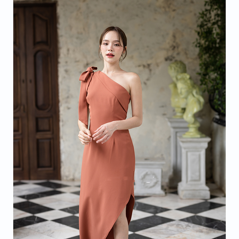 kudapy เดรสยาวสีชมพู/สีครีม/สีน้ำตาลอมส้ม ช่วงบนเป็นแบบปาดไหล่ข้างเดียวแต่งผ้าพับอก มีสายผูกโบว์ที่ไหล่ด้านขวาเพิ่มความหวาน เป็นกระโปรงทรงสอบ กระโปรงชายเฉียงเพิ่มความสวยชิค
