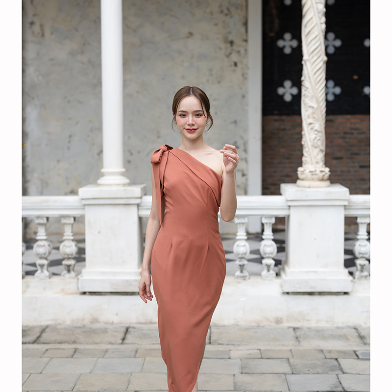 kudapy เดรสยาสีสีน้ำตาลอมส้ม/สีครีม ช่วงบนเป็นแบบปาดไหล่ข้างเดียวแต่งผ้าพับอกดูไม่เรียบจนเกินไป มีสายผูกโบว์ที่ไหล่ด้านขวาเพิ่มความหวาน