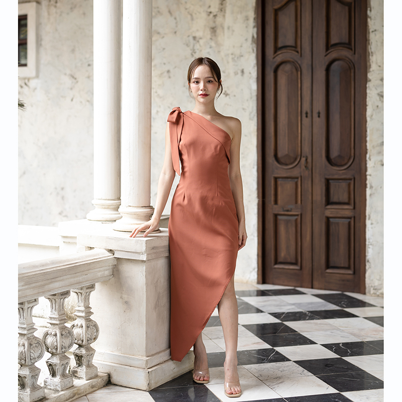 kudapy เดรสยาวสีชมพู/สีครีม/สีน้ำตาลอมส้ม ช่วงบนเป็นแบบปาดไหล่ข้างเดียวแต่งผ้าพับอก มีสายผูกโบว์ที่ไหล่ด้านขวาเพิ่มความหวาน เป็นกระโปรงทรงสอบ กระโปรงชายเฉียงเพิ่มความสวยชิค