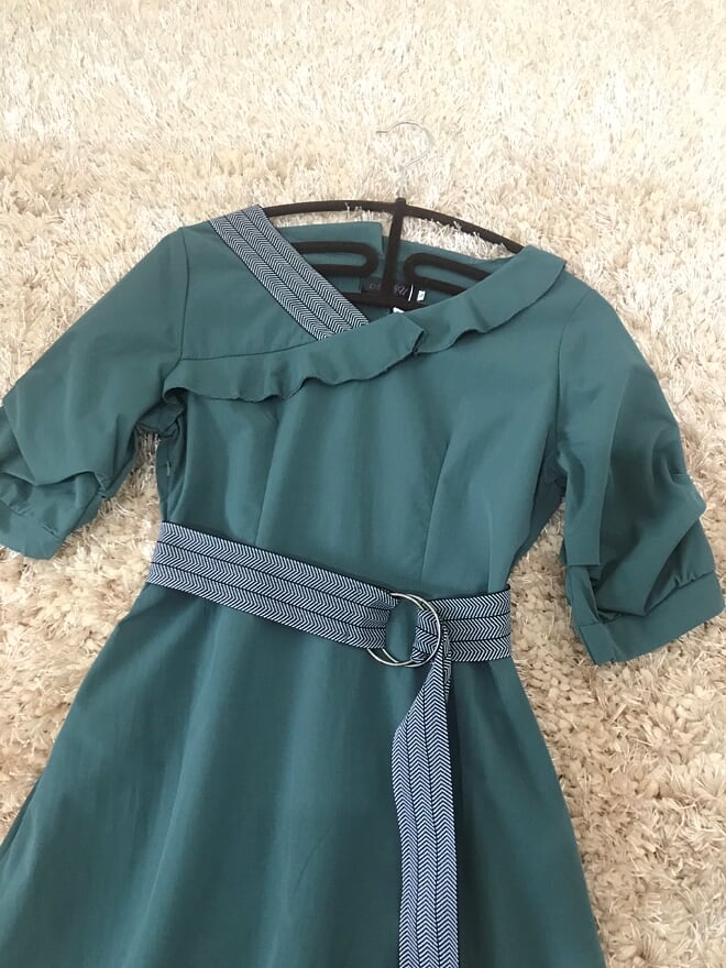 เดรสสั้นสีเขียว คอปาดกว้าง ผ้าคอตตอนผสม แต่งคอเสื้อข้างขวาลายเดียว มีเข็มขัดผูกเอวตามแบบ