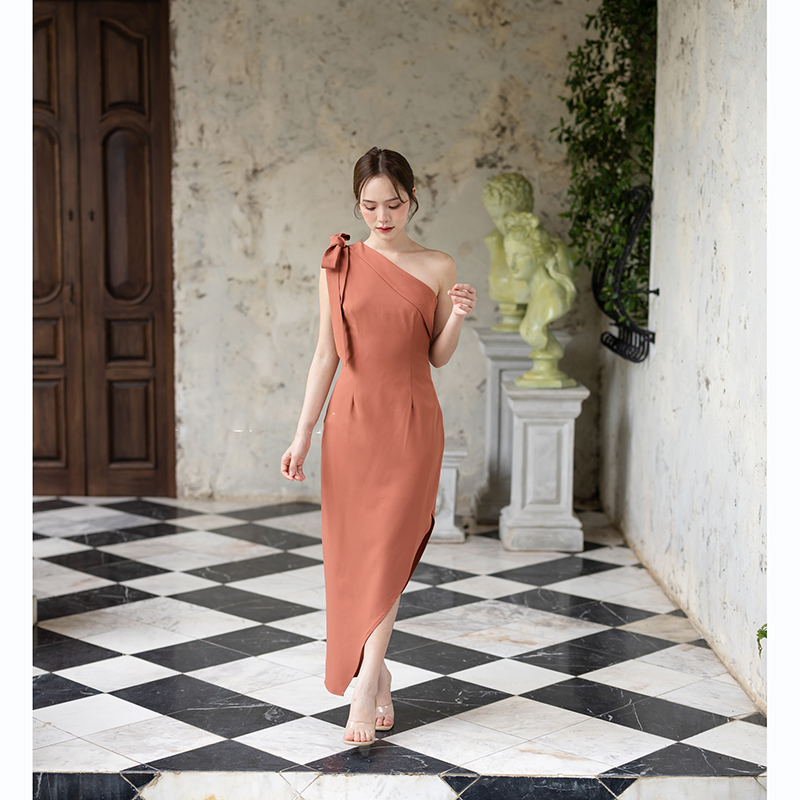 kudapy เดรสยาวสีชมพู/สีครีม/สีน้ำตาลอมส้ม ช่วงบนเป็นแบบปาดไหล่ข้างเดียวแต่งผ้าพับอก มีสายผูกโบว์ที่ไหล่ด้านขวาเพิ่มความหวาน เป็นกระโปรงทรงสอบ กระโปรงชายเฉียงเพิ่มความสวยชิค